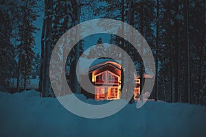 A night view of cozy wooden scandinavian cabin cottage chalet house covered in snow near ski resort in winter with the lights turn