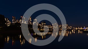 Night view of False Creek bay in the downtown of Vancouver, Canada with illuminated high-rise buildings reflected in water.