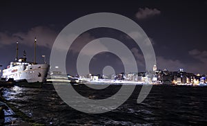 Night view of Galata bridge and Galata tower. Lights reflected in the sea and steamboat on the pier