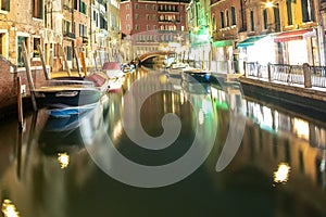 Night view of illuminated old buildings, floating boats and light reflections in canal water in Venice, Italy