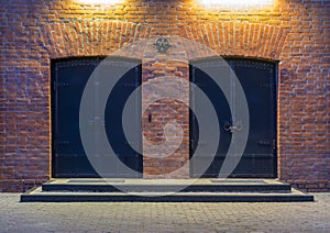Night view. Industrial building. Two large metal doors in a red brick building. The entrance to the warehouse. Facade