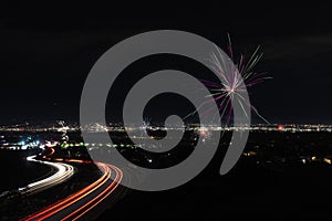 Night view of a road with bright traffic lights trails under the fireworks sky on July 4th, US