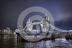 Night view of the skyline of London with a cruise ship passing under the lifted Tower Bridge