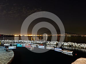 Night view of small pier with coloured boats on city lights