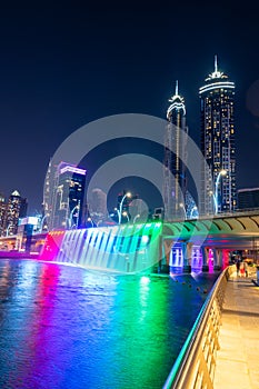 Night view to the Dubai Water Canal waterfall. Amazing rainbaw colors reflect over water.