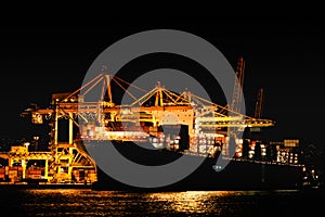 Night view of trieste harbor from the mediterranean sea. disembarkation of a container ship with yellow cranes