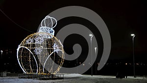 Night view of two silhouettes walking around a wonderful giant toy ball figure decorated by shining led lights. Concept