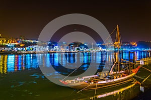 night view of a wooden boat used for transport of wine anchoring along riverside of Douro in Porto, Portugal