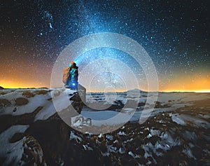 Night winter landscape a man with a backpack and a lantern on his head sits on a rock in the mountains in winter against