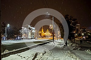 Night winter street during snowfall in the city with a view of the organ hall and Holy Trinity Church