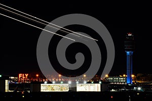 Nightime view of the Atlanta international airport with air traffic control and streaks of planes taking off over bright hangars