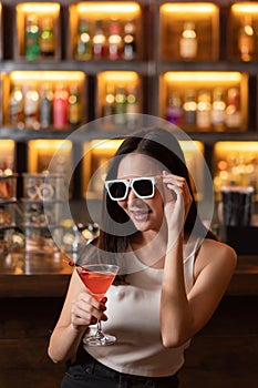 Nightlife concept a sexy girl wearing sunglasses looking mysterious with a straight face holding a drink with cherry on the top