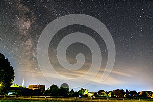 Nightscape of the sky full of stars trails and reflection of clouds above the houses and trees