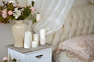 On the nightstand beside the bed is a vase with flowers and candles