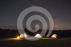 Nighttime camping under stars with glowing campfire and tents in a serene forest setting. Peaceful starry night concept.