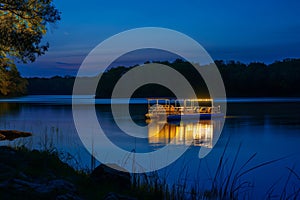 nighttime shot of litup pontoon boat floating on a tranquil lake