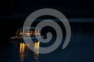 nighttime shot of litup pontoon boat floating on a tranquil lake
