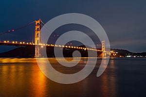 Nighttime view of Golden Gate Bridge reflected in the blurred water surface of San Francisco bay, California