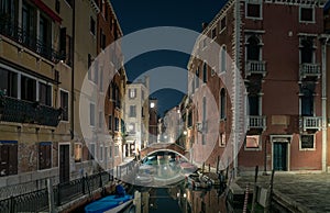 Nighttime view of a narrow Venetian canal and a bridge between buildings