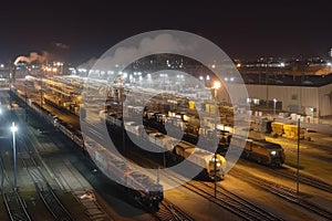 nighttime view of railway yard, with train engines and cars illuminated by bright lights