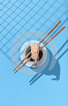 Nigiri prawn near soy sauce, with chopsticks on a blue background. Hard lighting and shadow. Traditional Japanese cuisine