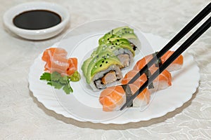 Nigiri salmon sushi in the foreground with chopsticks gripping it.