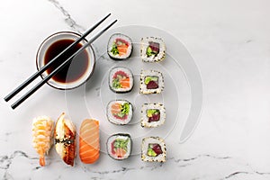 Nigiri sushi, maki rolls and soy sauce on a white stone background and chopsticks on the side.