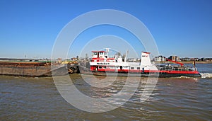 View on HGK pusher boat herkules vessel with cargo barge on river waal against blue sky