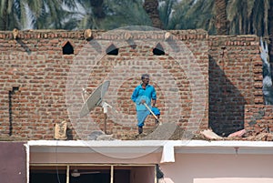 Nile River, near Aswnm, Egypt, February 21, 2017: Egyptian worker resting and fixing a roof with stones and sand, next to a satell