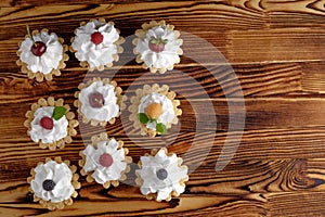 Nine cakes with protein cream and summer berries on wooden table.