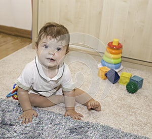 Nine months old baby sitting on the floor and playing with toys at home interior
