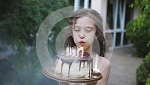 A nine-year-old girl blows out candles on a birthday cake in the backyard. Close-up slow motion shooting blowing out