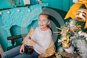 A nine-year-old girl sits in a rocking chair in front of the fireplace next to a Christmas tree and holds a large lantern in her