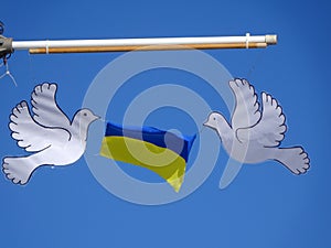 Nitaure, LATVIA - MARCH 10, 2022: Two white doves of peace hold the Ukrainian flag on a blue sky background