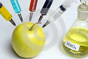 Nitrates, pesticides, fungicides and other chemicals are injected into a green apple with a syringe. The concept of GMO