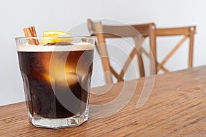 Nitro cold brew coffee with ice, cinnamon and lemon on wooden table and chairs set as a special drink menu ready to serve for the