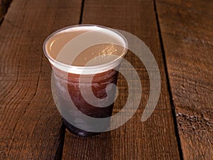 Nitrogen infused cold brew coffee in a clear plastic cup on a wood table.