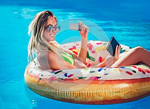 Njoying suntan Woman in bikini on the inflatable mattress in the swimming pool using digital tablet and credit card.