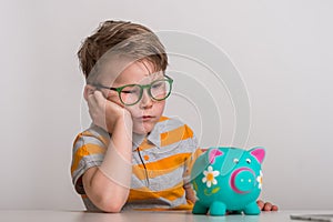 No cash money. Little caucasian kid banking money on piggy bank as wealth savings with angry face, negative sign showing