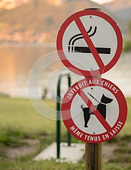 no dogs sign and no smoking sign in a public park with a lake in the background