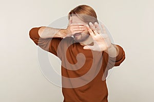 No, don`t want to look! Portrait of confused man covering eyes and raising hand to stop, feeling stressed afraid