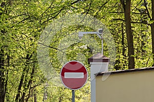 No entry Road sign and the security camera on the background of green trees