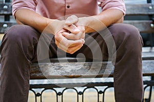 No face visible. Man spend time sitting on the bench with hands put together wearing pink shirt. Overpassing problems