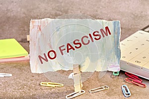 no fascism text written on paper next to scattered paper clips, calculator, adhesive paper