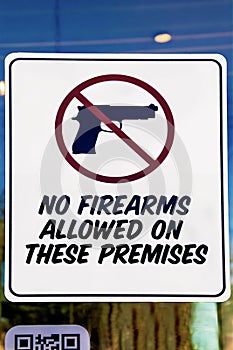 No firearms allowed on these premises sign closeup on door to US glass business with reflections