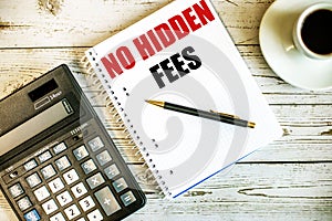 NO HIDDEN FEES written on white paper near coffee and calculator on a light wooden table. Business concept