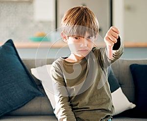 No kid enjoys being alone and hungry. Portrait of a cute little boy showing the thumbs down while sitting on a sofa at