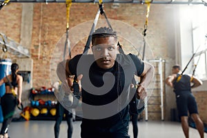 No Limits. Athletic young man doing fitness TRX training exercises at industrial gym. Push-up, group workout concept
