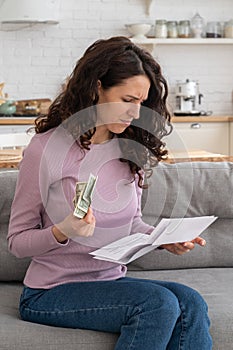 Sad young girl holding last cash money feeling anxiety about debt or bankruptcy, sitting at home.