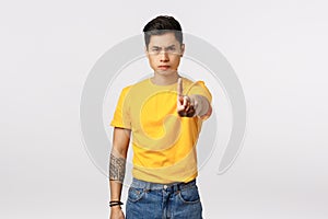 No more, stop it. Serious-looking determined young handsome asian guy with tattoos, extand arm and shaking index finger